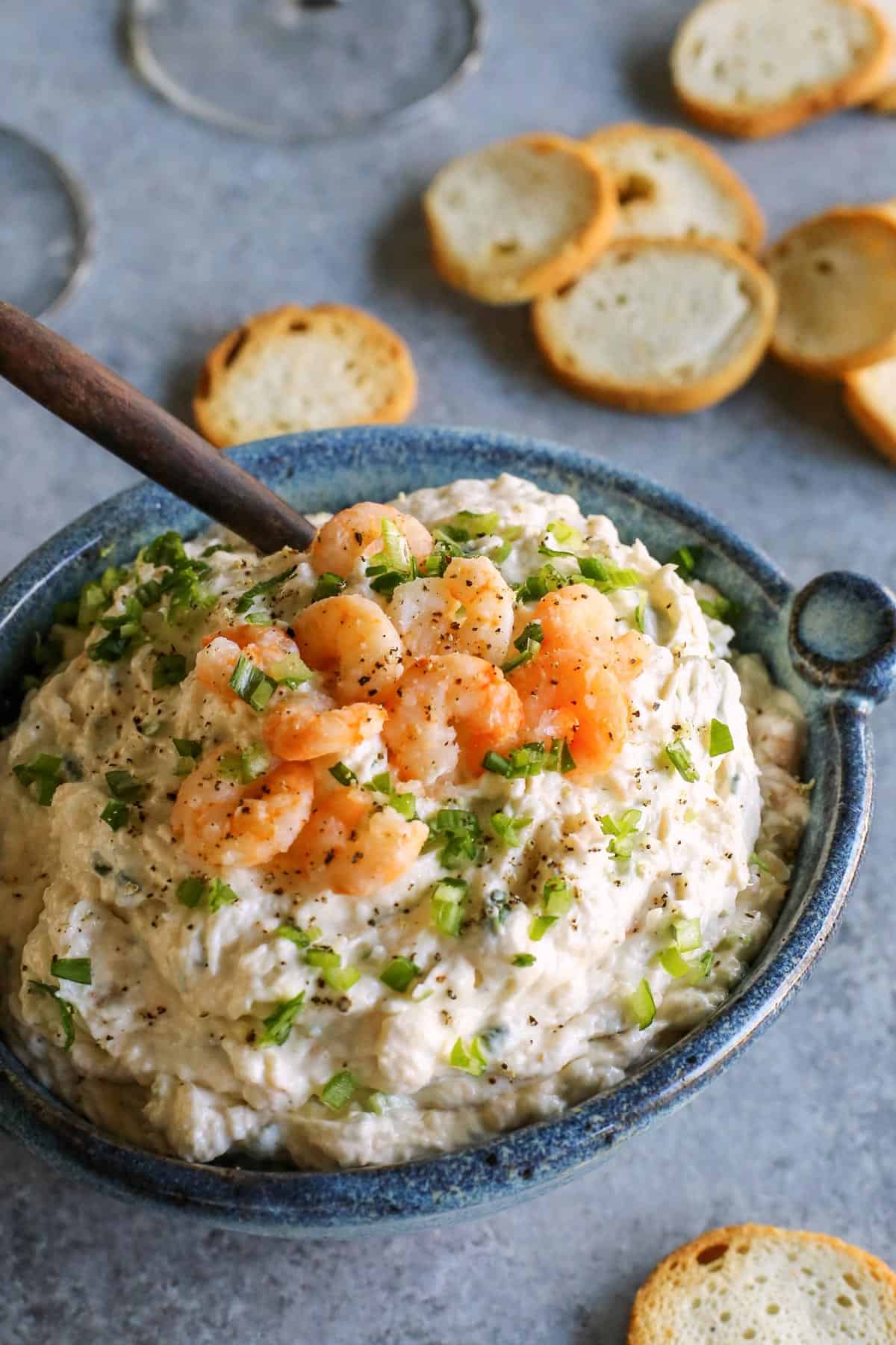 This shrimp dip recipe is an easy appetizer, made with just a few ingredients. It's thick and creamy, and full of tender, juicy shrimp! Blue bowl filled with cold shrimp dip, plus baguette crackers for dipping.