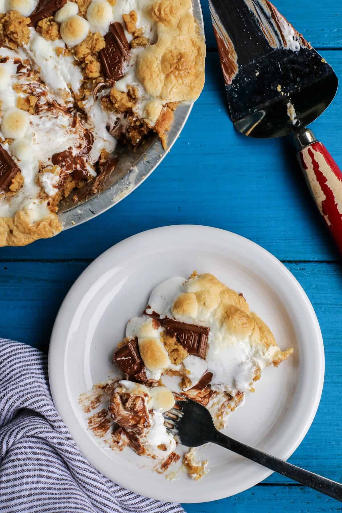 Gooey, chocolatey, and utterly delicious, this S'mores Pie allows you to enjoy the flavors of the classic summertime treat any time of the year. No campfire required! a slice of S'mores Pie on a white plate
