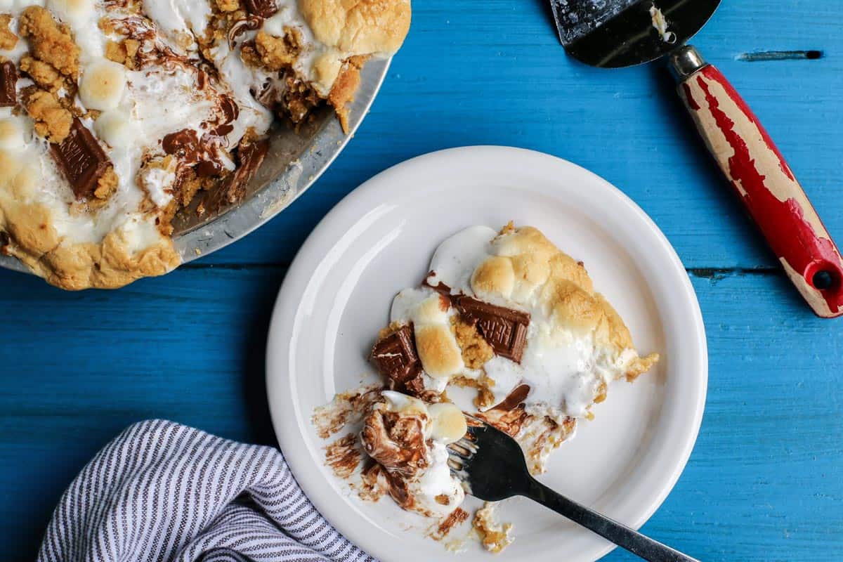 Gooey, chocolatey, and utterly delicious, this S'mores Pie allows you to enjoy the flavors of the classic summertime treat any time of the year. No campfire required! S'mores Pie slice on a white plate