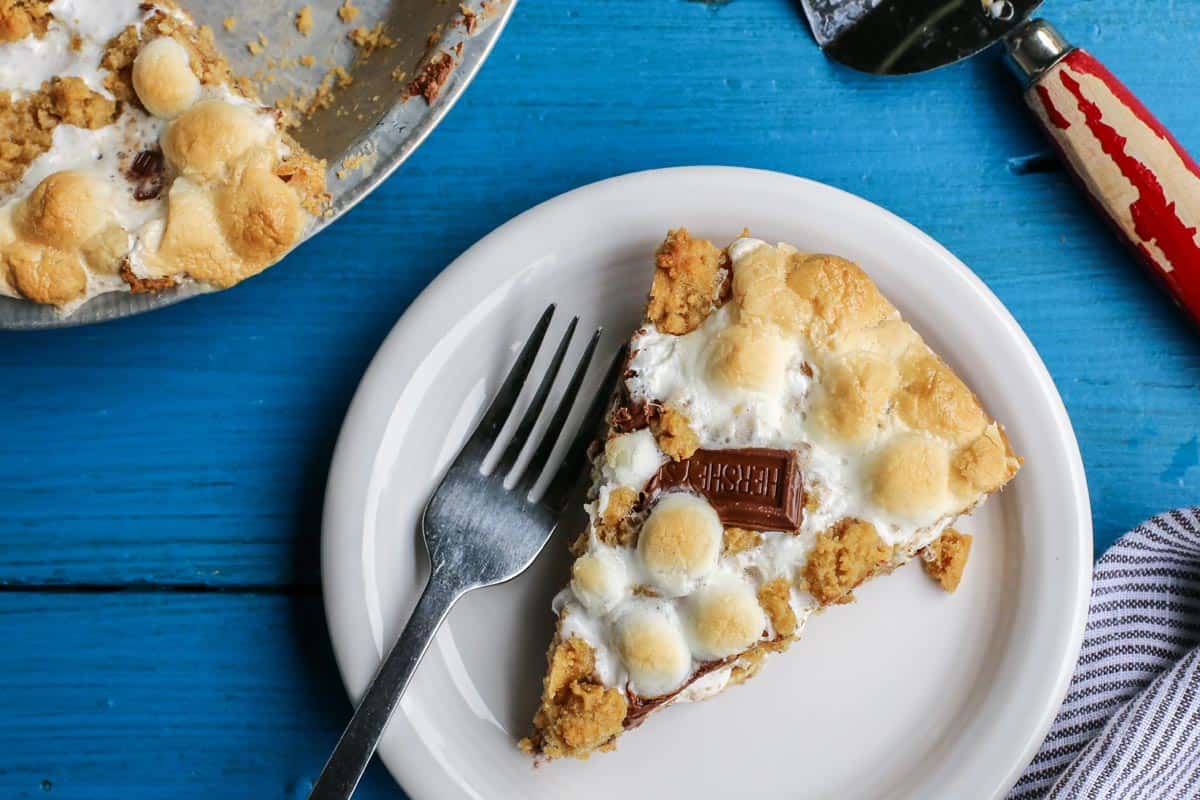 Gooey, chocolatey, and utterly delicious, this S'mores Pie allows you to enjoy the flavors of the classic summertime treat any time of the year. No campfire required! S'mores Pie slice taken out of whole. pie