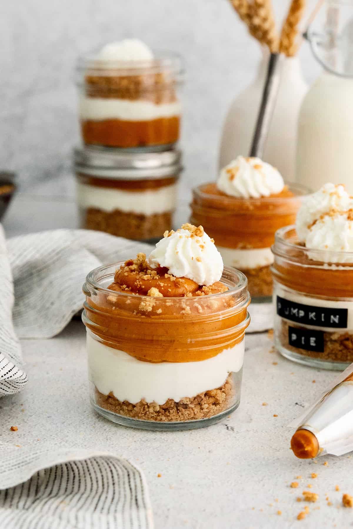This no-bake pumpkin pie in a jar recipe with warm spices, tangy cheesecake, spiced pumpkin, and whipped cream is great for the holidays. Layered pumpkin pie in a jar with whipped cream and chocolate shavings on top.