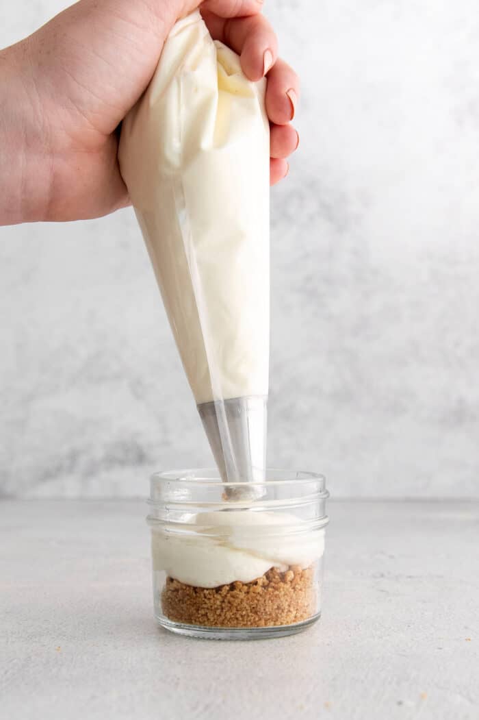 This no-bake pumpkin pie in a jar recipe with warm spices, tangy cheesecake, spiced pumpkin, and whipped cream is great for the holidays. Piping the cream cheese mixture into the jar.