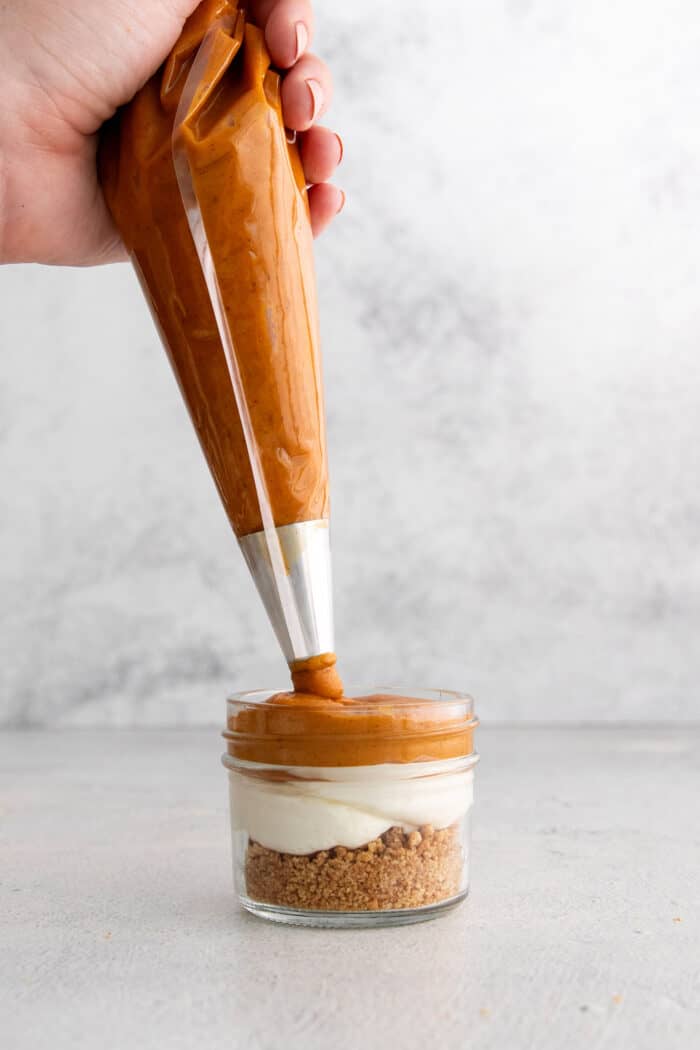 This no-bake pumpkin pie in a jar recipe with warm spices, tangy cheesecake, spiced pumpkin, and whipped cream is great for the holidays. Piping the pumpkin mixture layer.