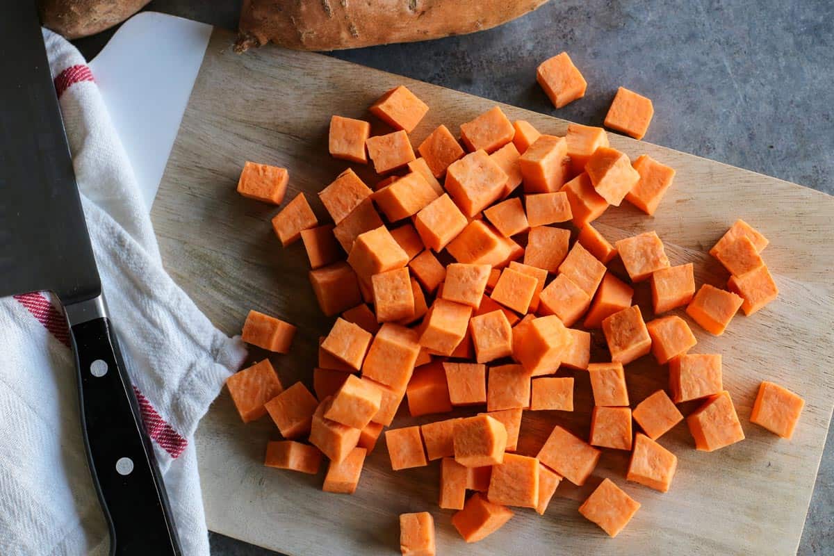 With shredded chicken, chunks of sweet potato, and creamy coconut milk, this warming Thai chicken soup comes together in under an hour! Overhead view of cubed sweet potatoes on cutting board.
