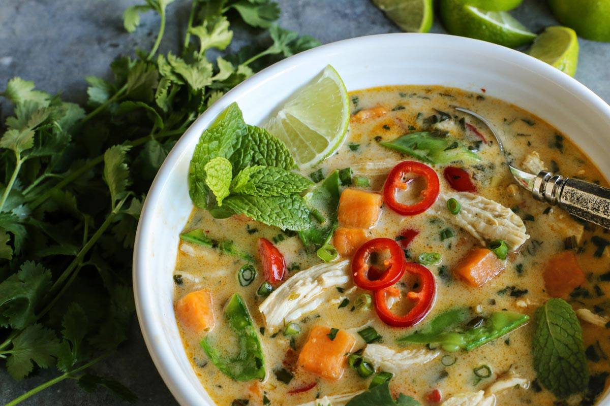 With shredded chicken, chunks of sweet potato, and creamy coconut milk, this warming Thai chicken soup comes together in under an hour! Thai Chicken Soup in a white bowl garnished with fresh mint and sliced chilies.