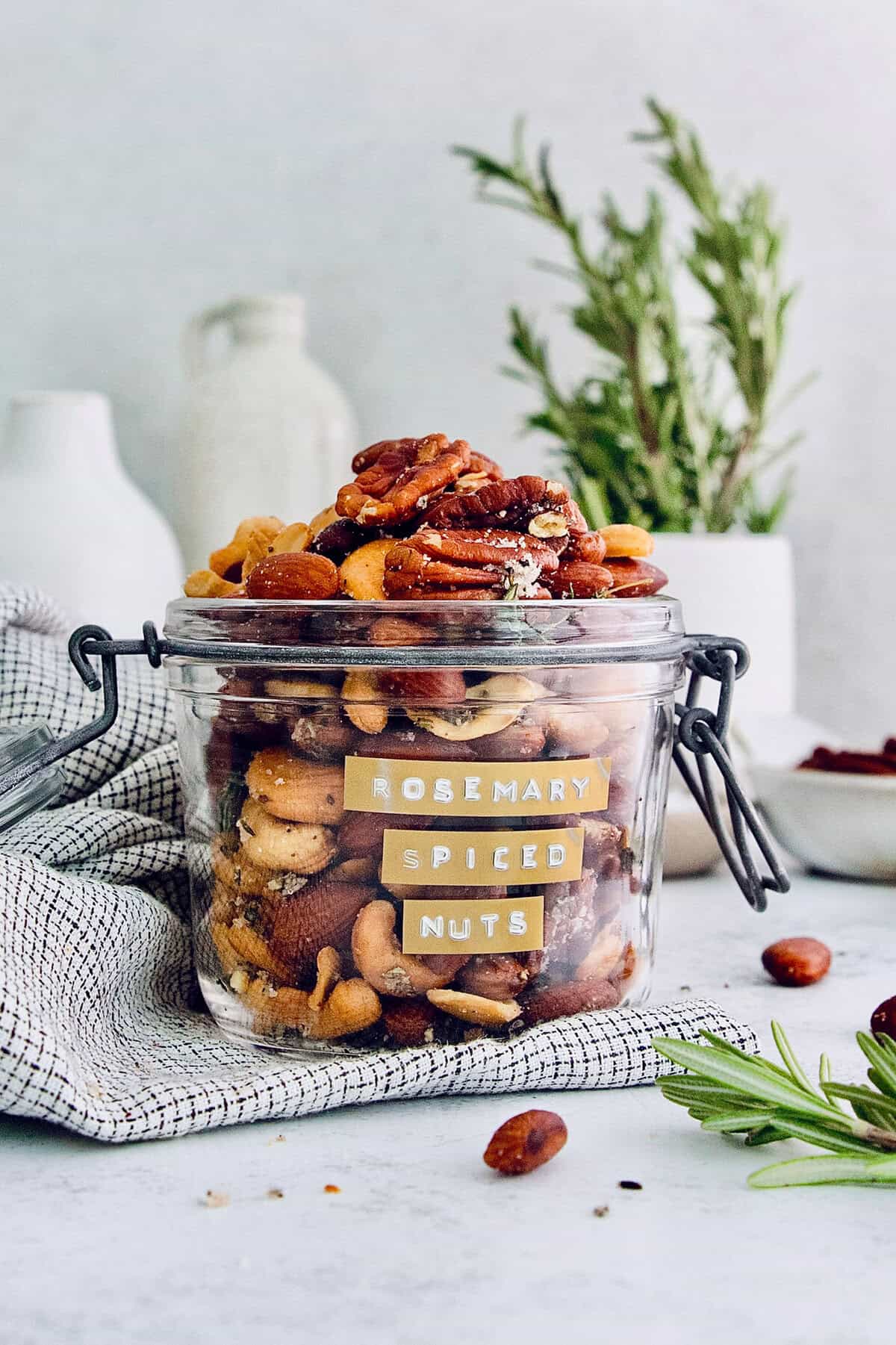 This homemade, baked spiced nuts recipe with herb-infused olive oil, cumin, spicy cayenne, and sugar is an easy holiday appetizer. Baked mixed nuts with herbs and spices in a glass jar.