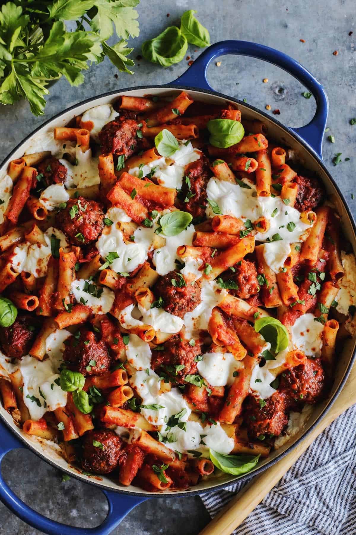 A large blue casserole dish holds herb-garnished meatball pasta casserole/