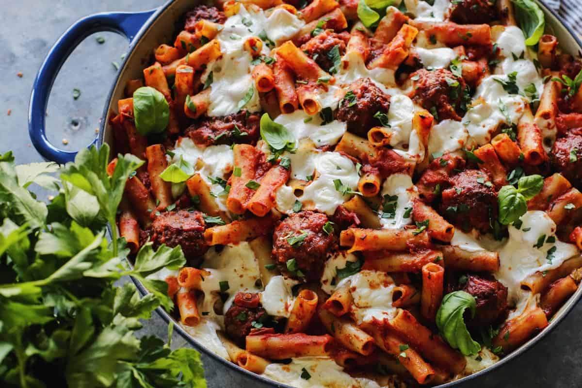 A pan of cheesy meatball pasta casserole topped with fresh herbs.