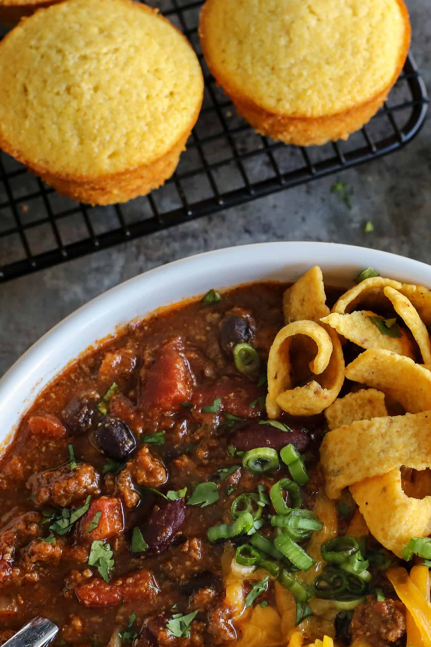 This Slow Cooker Chili recipe has been in my family for years! It's an easy, homemade chili cooked in the crockpot & packed with flavor. A bowl of slow cooker chili near some cornbread muffins
