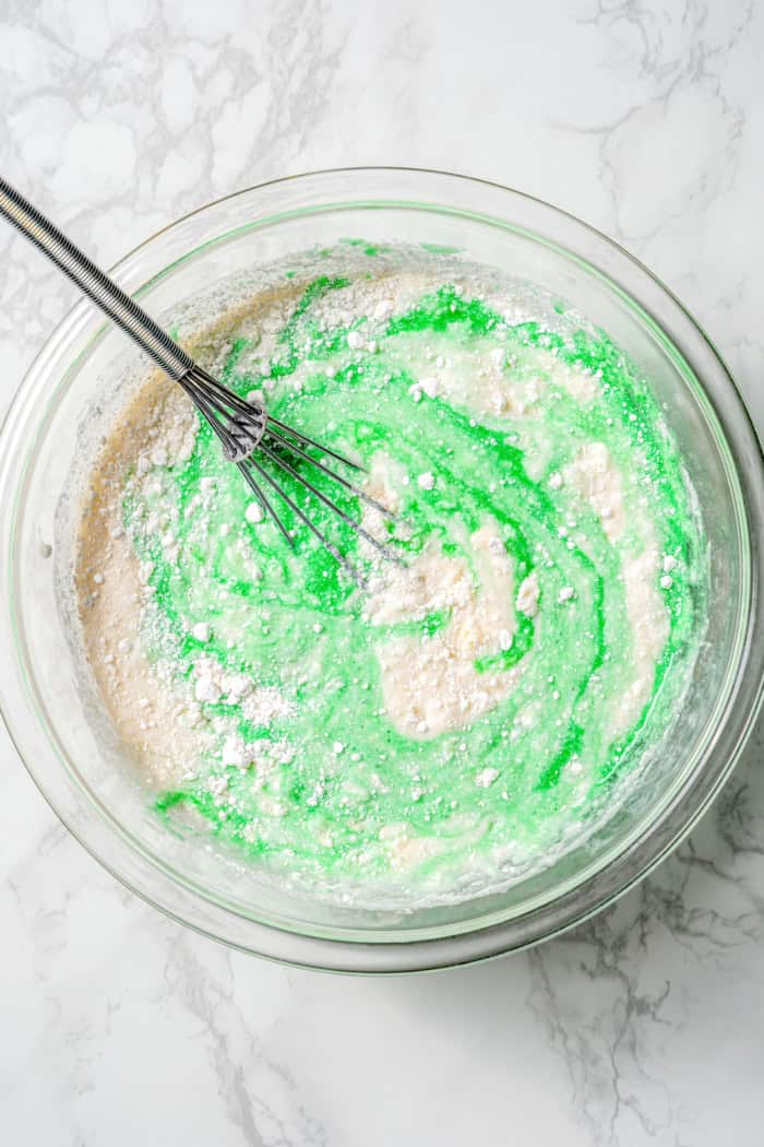 This Grasshopper Cake has layers of moist mint cake, chocolate fudge, and creme de menthe-infused whipped cream. So easy too! Mixing cake batter in bowl with whisk