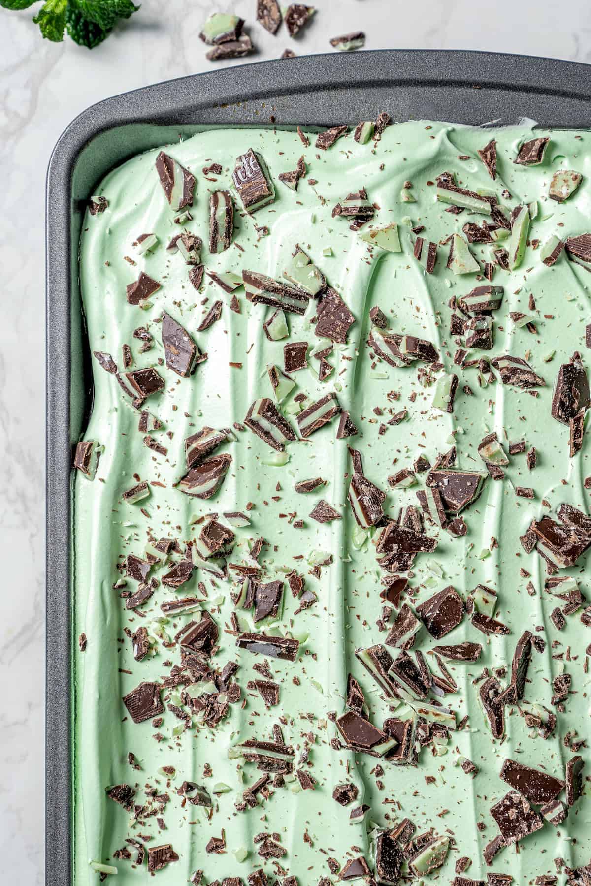 This Grasshopper Cake has layers of moist mint cake, chocolate fudge, and creme de menthe-infused whipped cream. So easy too! Grasshopper cake in pan before slicing