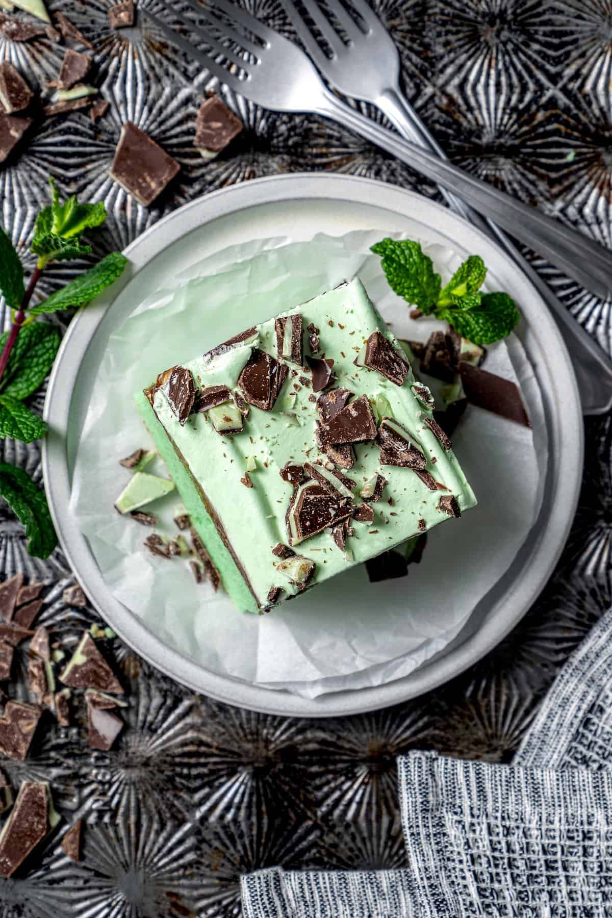 This Grasshopper Cake has layers of moist mint cake, chocolate fudge, and creme de menthe-infused whipped cream. So easy too! Top-down view of grasshopper cake on plate
