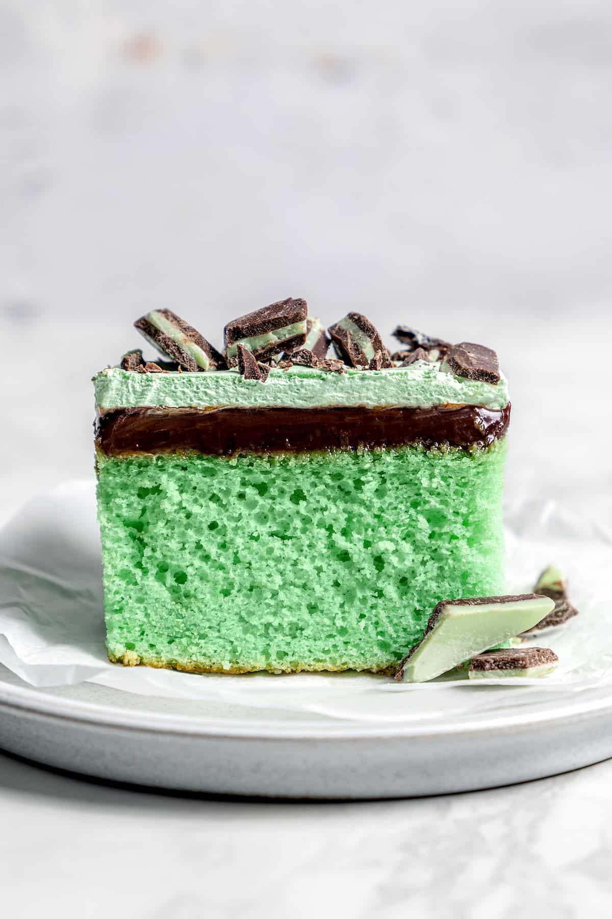 This Grasshopper Cake has layers of moist mint cake, chocolate fudge, and creme de menthe-infused whipped cream. So easy too! Slice of grasshopper cake on plate