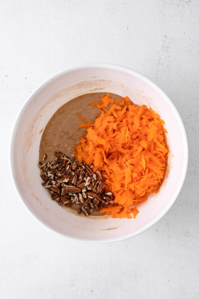 This classic carrot cake recipe is moist, perfectly spiced, and baked in a single layer, topped with creamy homemade cream cheese frosting. Cake batter, shredded carrots, and chopped nuts in a white bowl