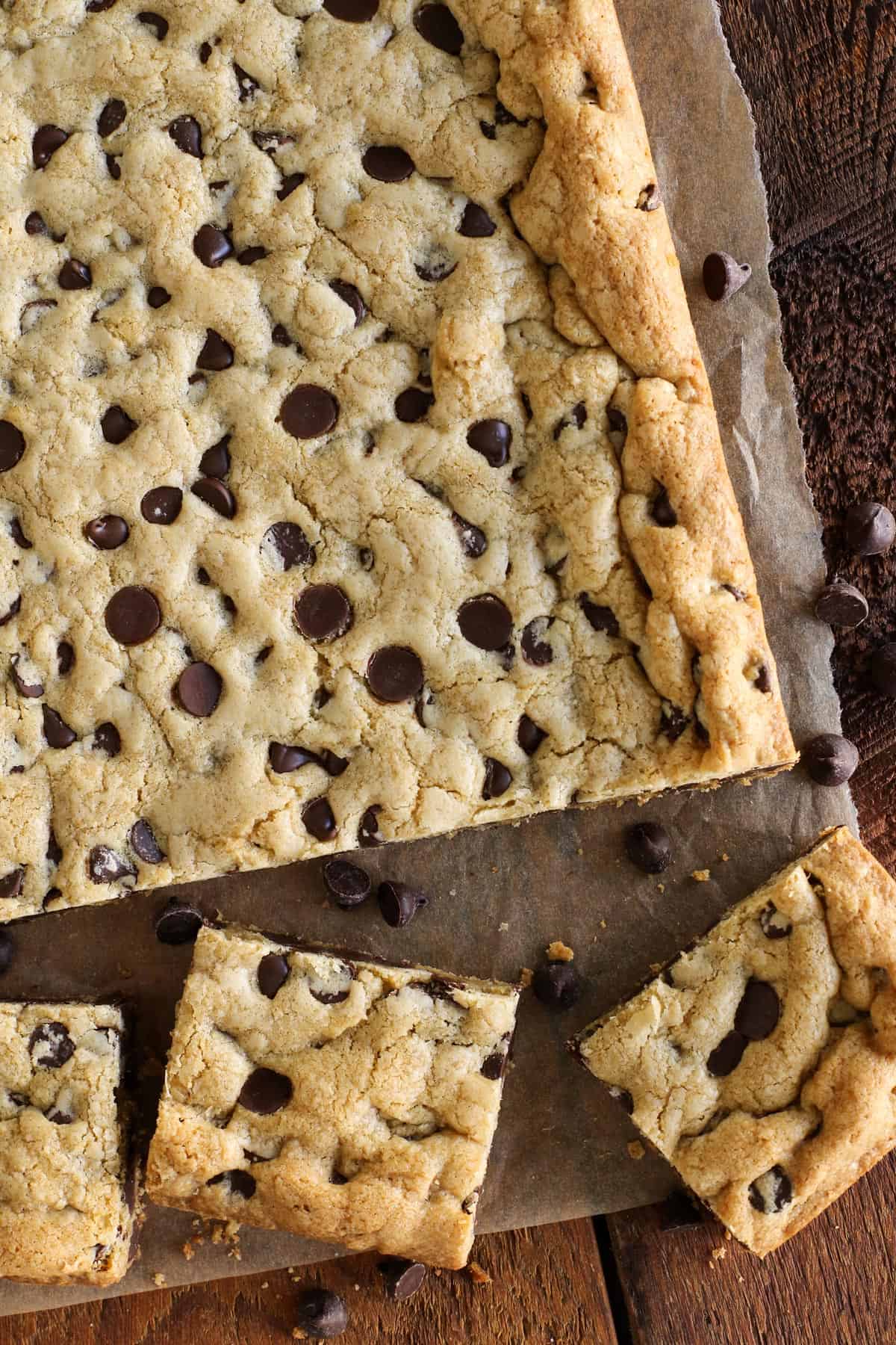 These soft and chewy Chocolate Chip Cookie Bars are just like your favorite chocolate chip cookies but baked in one pan. A few chocolate chip cookie bars are cut from the whole pan of bars with chocolate chips scattered around them.