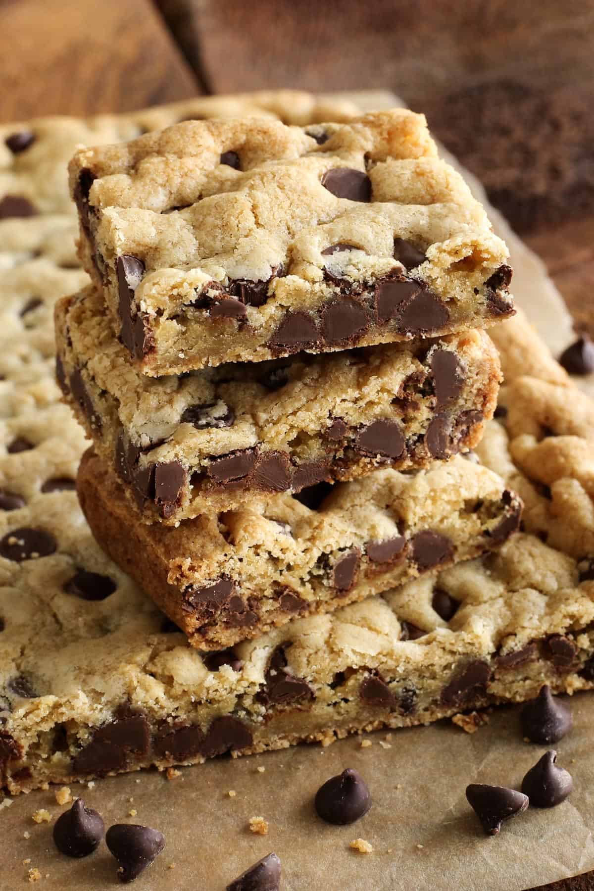 These soft and chewy Chocolate Chip Cookie Bars are just like your favorite chocolate chip cookies but baked in one pan. A stack of chocolate chip cookie bars is piled on top of the tray of bars.