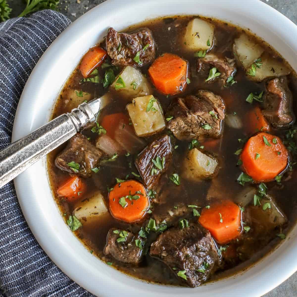 This traditional Irish beef stew is extra hearty, with tender beef and vegetables simmered in a rich beef broth with Irish Guinness beer. Overhead view of Irish beef stew with potatoes and carrots in a bowl with a spoon.