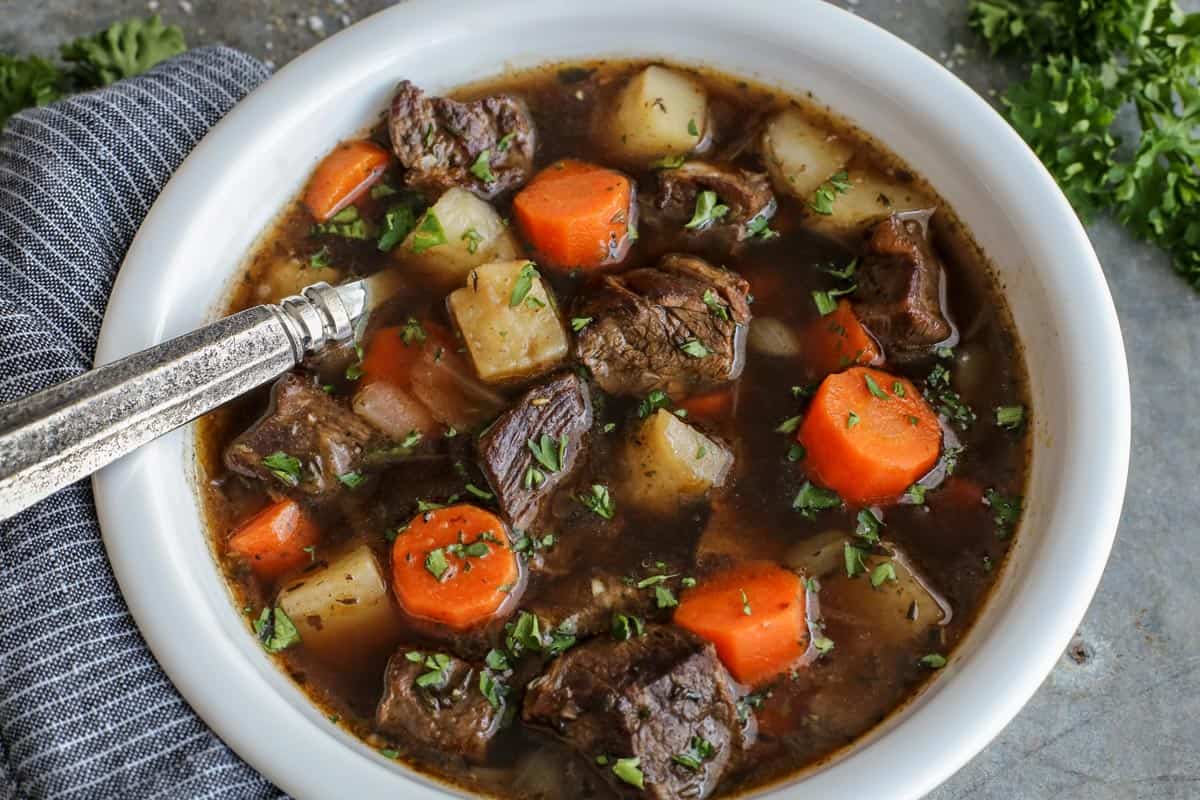 This traditional Irish beef stew is extra hearty, with tender beef and vegetables simmered in a rich beef broth with Irish Guinness beer. Overhead view of Irish beef stew with potatoes and carrots in a bowl with a spoon.