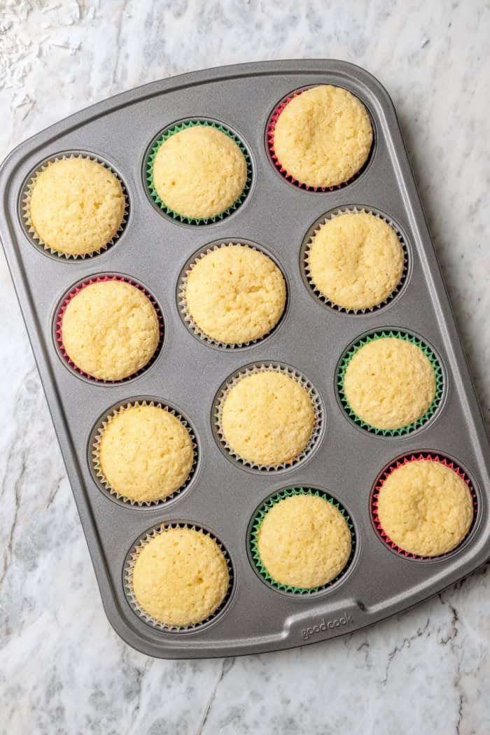 These coconut cupcakes are moist and full of coconut flavor — and just wait until you sink your teeth into the coconut buttercream frosting! Overhead view of coconut cupcakes in pan after baking