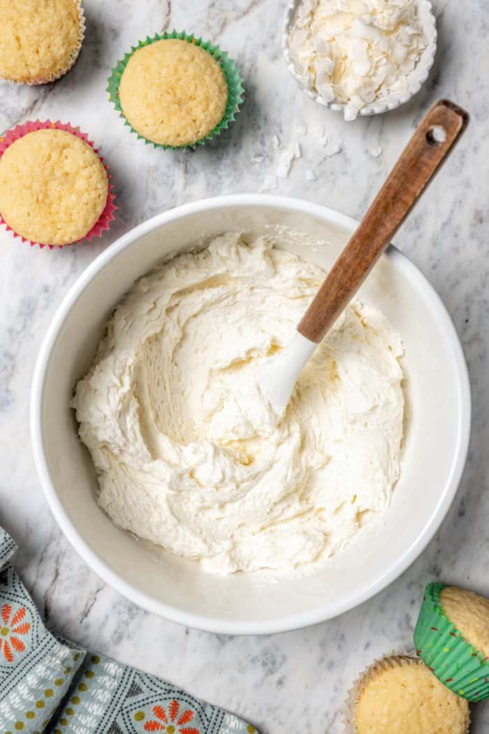 These coconut cupcakes are moist and full of coconut flavor — and just wait until you sink your teeth into the coconut buttercream frosting! Overhead view of coconut buttercream in mixing bowl with rubber spatula