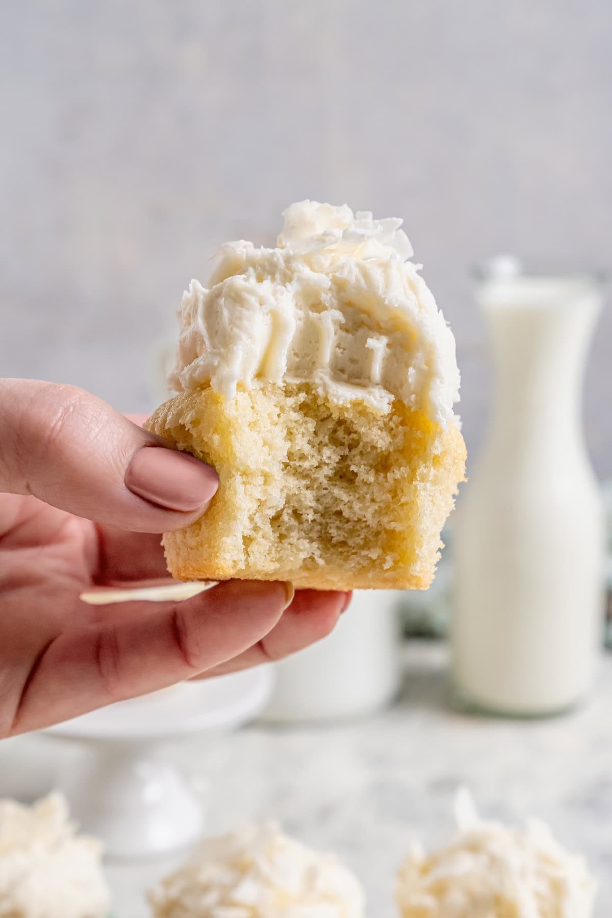 These coconut cupcakes are moist and full of coconut flavor — and just wait until you sink your teeth into the coconut buttercream frosting! Hand holding bitten coconut cupcake, showing fluffy texture