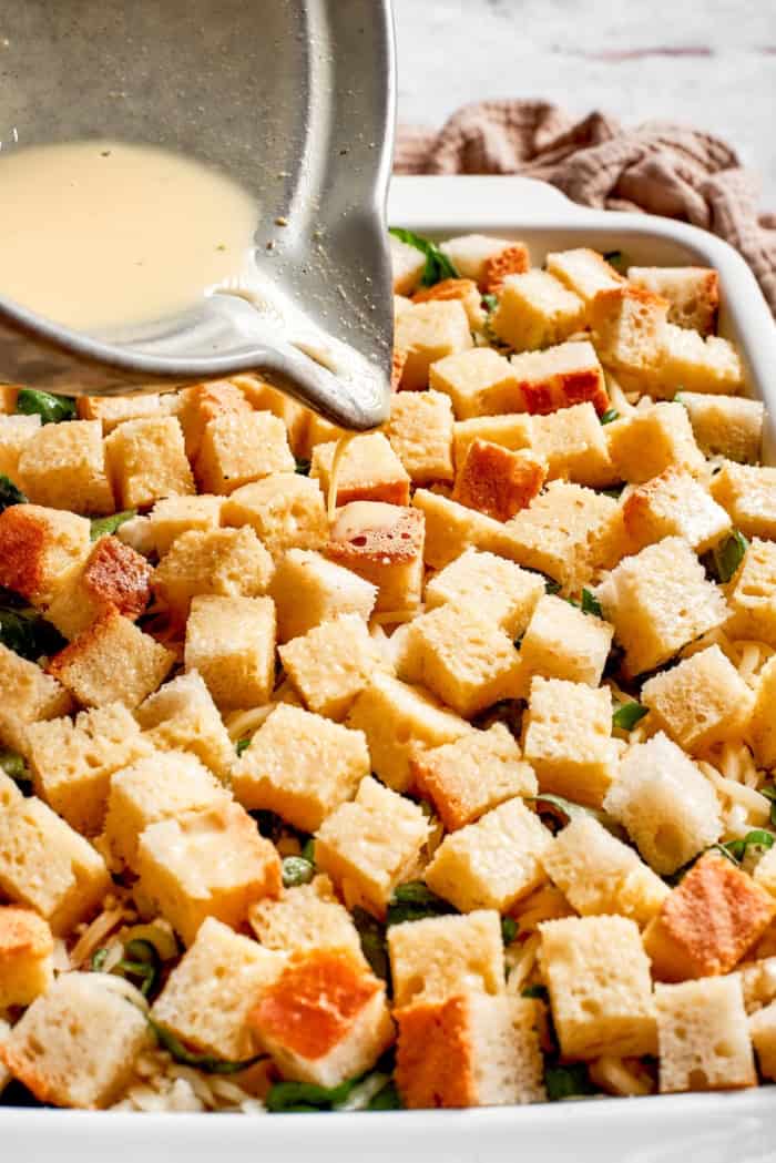 Pouring egg custard mixture into casserole dish with bread, cheese, and fillings
