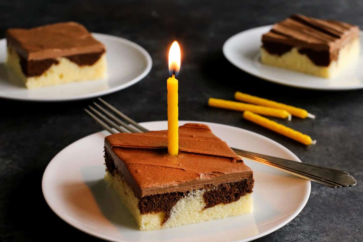This Easy Marble Cake Recipe features a moist chocolate and vanilla sheet cake slathered with a rich & creamy chocolate buttercream frosting. piece of marble cake with a yellow candle