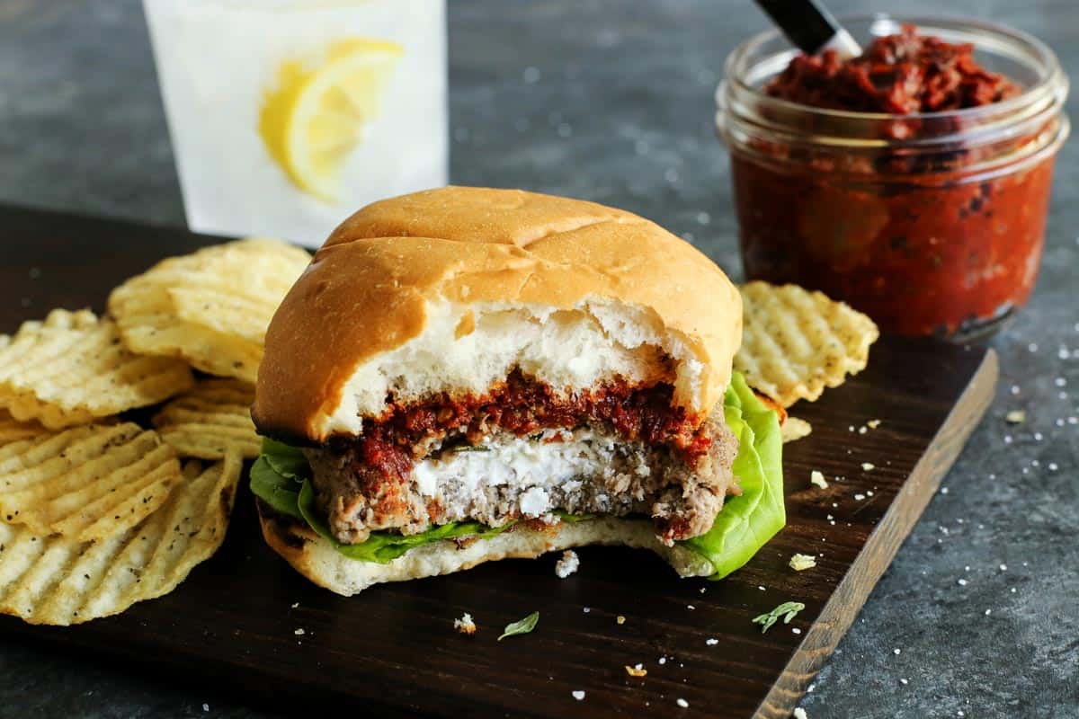 Ground Turkey Burgers feature juicy turkey patties stuffed with creamy, tangy goat cheese plus lots of fresh lemon and herbs. A turkey burger is served alongside chips, with a bite taken out to show the goat cheese inside.