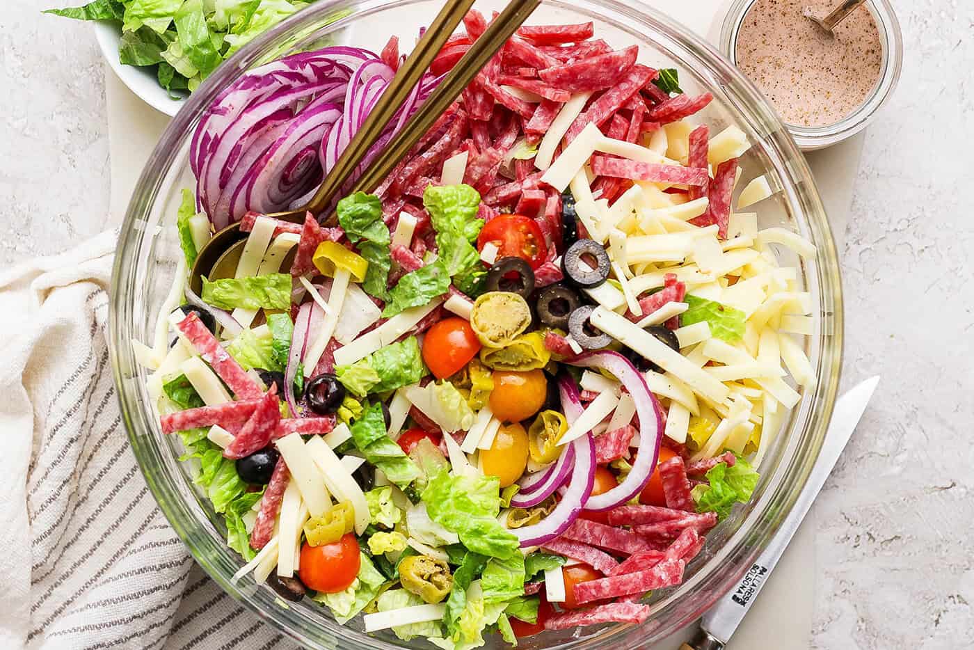 This Italian Chopped Salad is loaded with fresh veggies, salami, provolone, pepperoncini, and olives for a flavorful, satisfying meal! Overhead view of Italian chopped salad in glass bowl