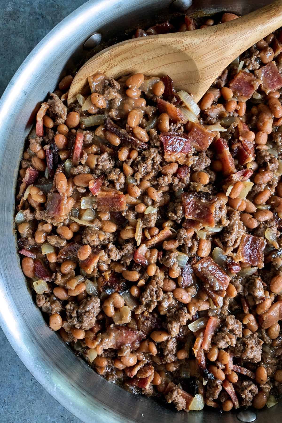 Made with bacon, ground beef, and baked beans, these easy Cowboy Beans are a hearty and flavorful side dish. They're the perfect accompaniment to anything off the grill and ideal for casual gatherings and potlucks too! skillet of cowboy beans with bacon and ground beef