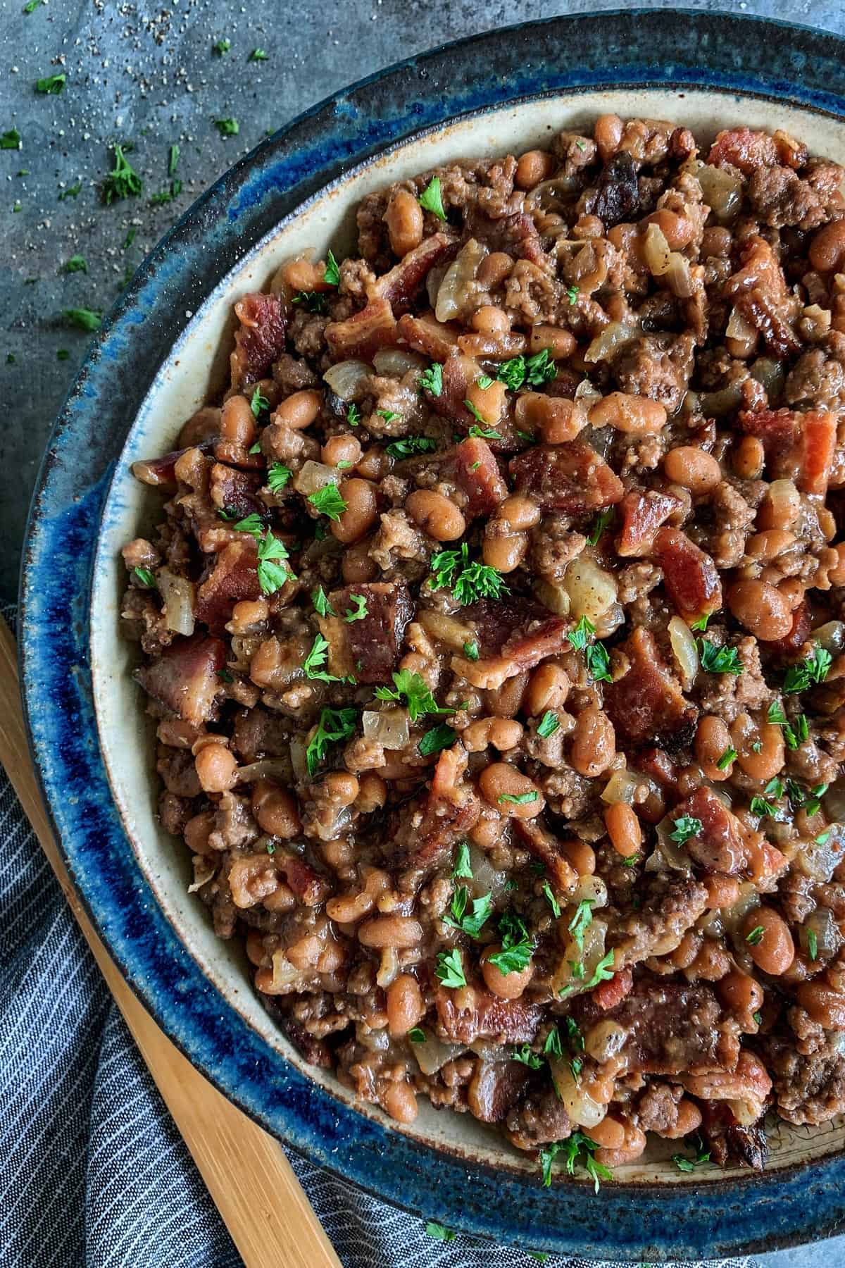Made with bacon, ground beef, and baked beans, these easy Cowboy Beans are a hearty and flavorful side dish. They're the perfect accompaniment to anything off the grill and ideal for casual gatherings and potlucks too! a bowl of baked beans with bacon and ground beef