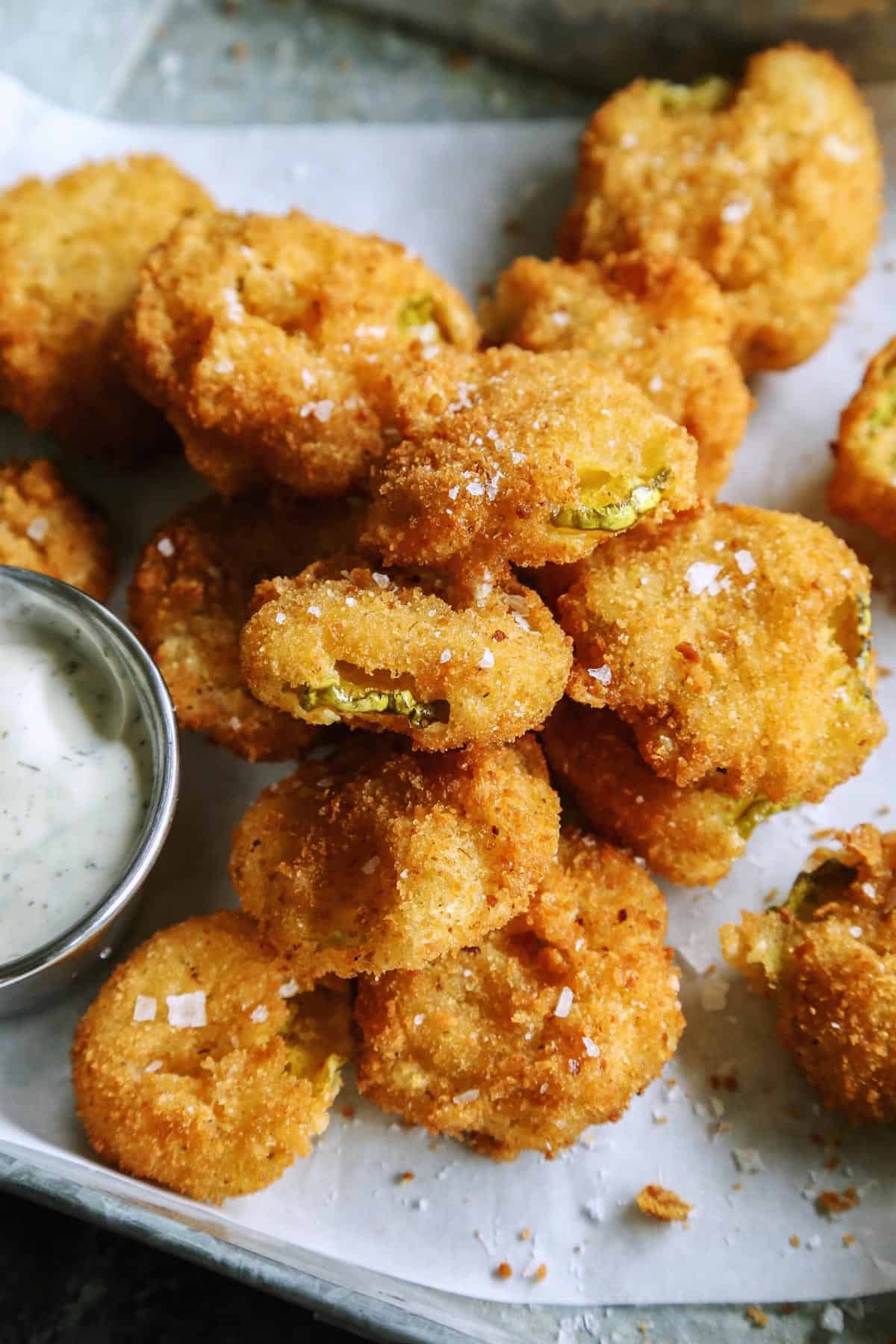 Enjoy your favorite fair food at home with these easy Fried Pickles. Dill pickles are dipped in a perfectly seasoned batter and quickly fried. fried pickles with dip on a tray
