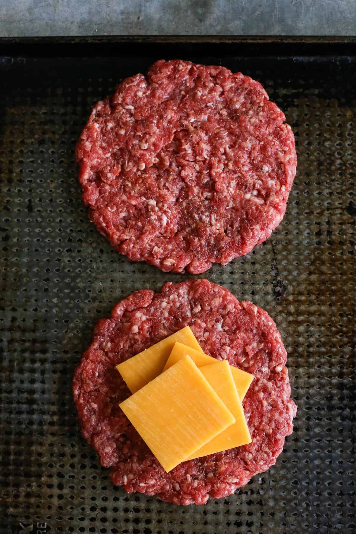 A Juicy Lucy burger is a juicy patty stuffed with molten, melty cheese. Served on a low-carb lettuce wrap or bun with your favorite toppings! a sheet pan with hamburger patties and slices of cheese