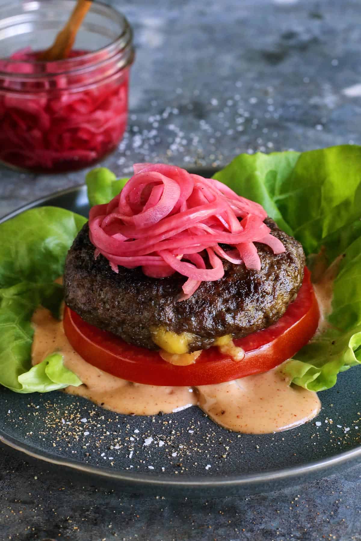 A Juicy Lucy burger is a juicy patty stuffed with molten, melty cheese. Served on a low-carb lettuce wrap or bun with your favorite toppings! cheese stuffed burger topped with pickled red onions