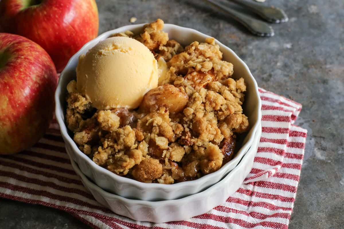 An easy apple crisp recipe with delicious apple filling and a crispy old-fashioned buttery oats topping. It's one of the best apple desserts! Apple crisp in a white ramekin with a scoop of ice cream