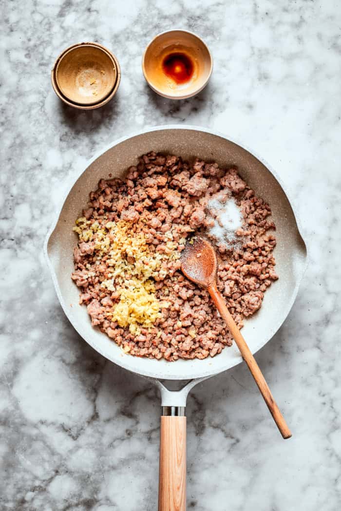 This easy Egg Roll in a Bowl recipe is loaded with ground pork, cabbage and carrots. Served with crispy wonton strips and a tasty Asian sauce! Overhead view of seasonings added to browned pork in skillet