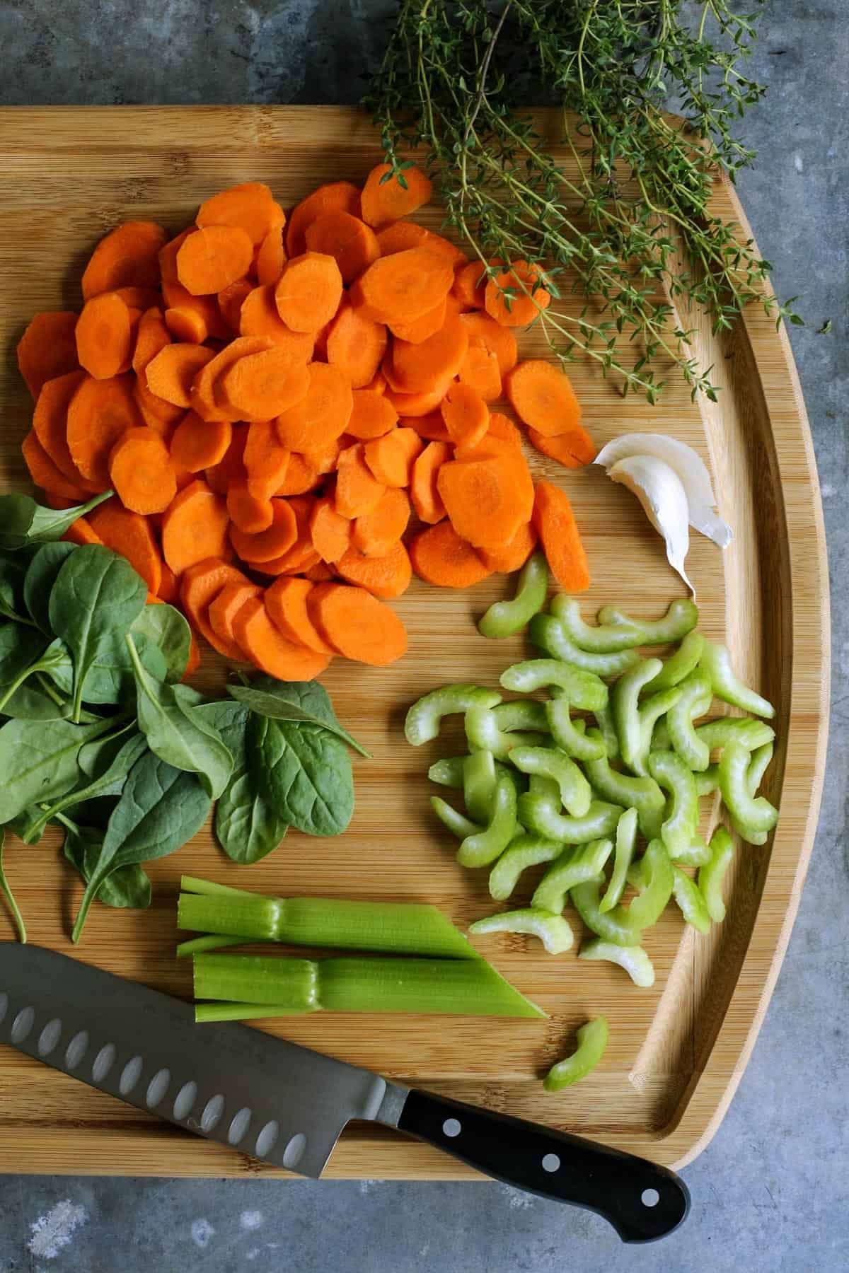 Made with leftover turkey and cheese tortellini, this Italian turkey tortellini soup is full of warm and cozy comfort. Ready in 30 minutes! fresh carrots, celery, garlic, spinach, and thyme on cutting board with chef's knife