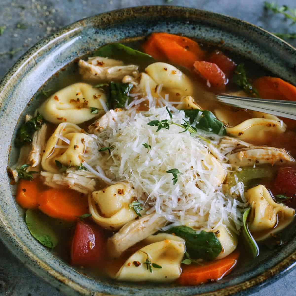Made with leftover turkey and cheese tortellini, this Italian turkey tortellini soup is full of warm and cozy comfort. Ready in 30 minutes! turkey tortellini soup in blue pottery bowl, with fresh Parmesan and herbs
