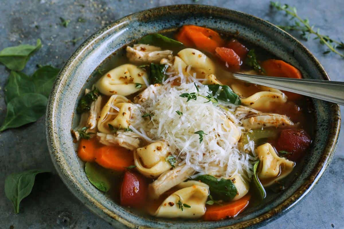 Made with leftover turkey and cheese tortellini, this Italian turkey tortellini soup is full of warm and cozy comfort. Ready in 30 minutes! turkey tortellini soup in blue pottery bowl, with fresh Parmesan and herbs