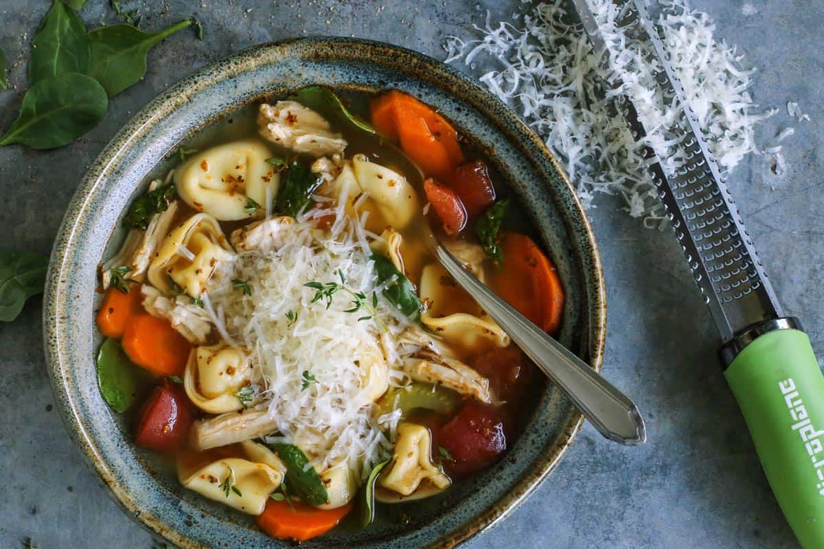 Made with leftover turkey and cheese tortellini, this Italian turkey tortellini soup is full of warm and cozy comfort. Ready in 30 minutes! turkey tortellini soup in blue pottery bowl, with freshly grated Parmesan