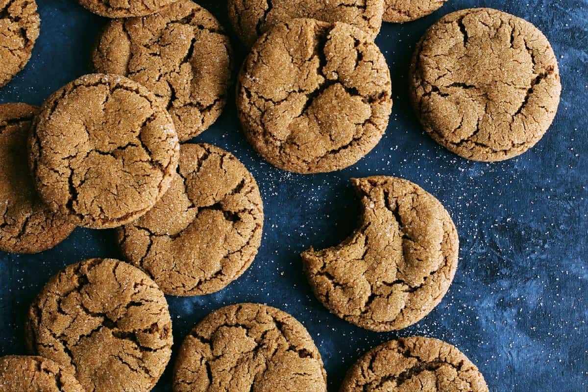 a batch of ginger molasses cookies on a dark blue background, one cookie has a big bite out of it