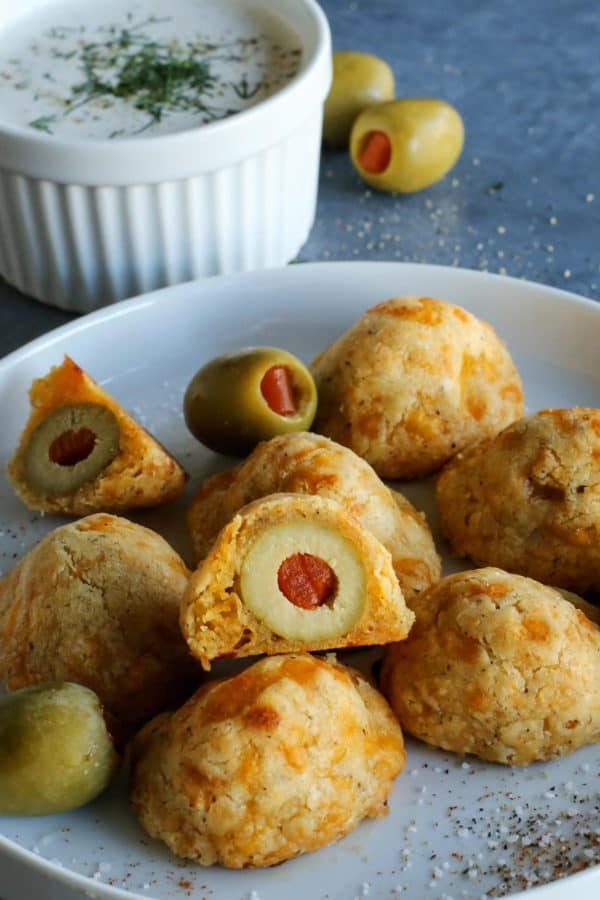 Olive Cheese Balls feature flaky, tender, cheesy dough that surrounds a warm and briny olive for a fun and easy appetizer. olives surrounded by cheesy dough, on a white plate