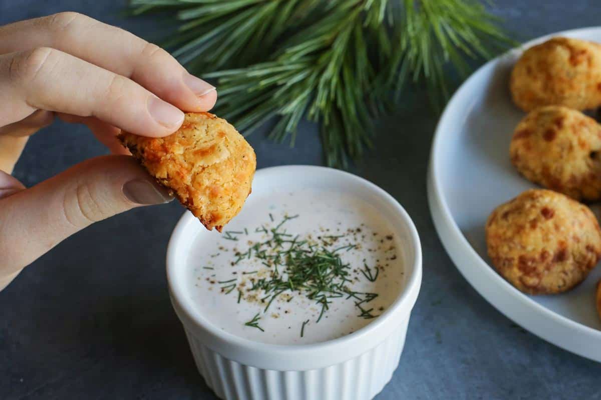 Olive Cheese Balls feature flaky, tender, cheesy dough that surrounds a warm and briny olive for a fun and easy appetizer. dipping a baked olive cheese ball into buttermilk ranch dip