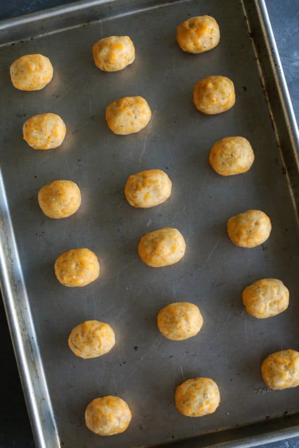 Olive Cheese Balls feature flaky, tender, cheesy dough that surrounds a warm and briny olive for a fun and easy appetizer. olives wrapped in cheese dough, lined up on a rimmed baking pan