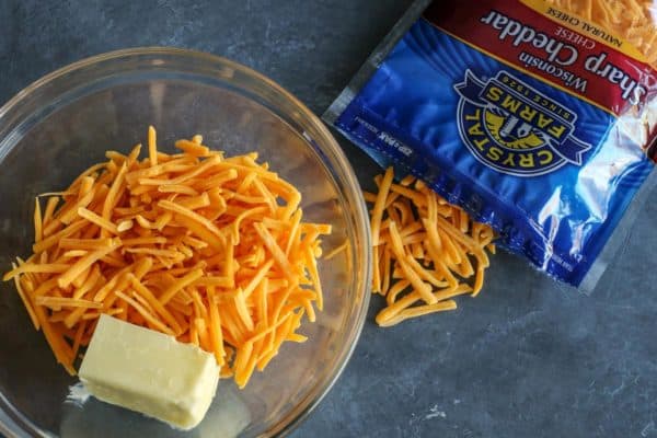 Olive Cheese Balls feature flaky, tender, cheesy dough that surrounds a warm and briny olive for a fun and easy appetizer. shredded sharp cheddar cheese and butter in a clear bowl, a package of Crystal Farms Sharp Cheddar on the side