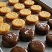 Ritz sandwich cookies with peanut butter inside, some are dipped in chocolate, some are sprinkled with sea salt flakes, all lined up on a rimmed pan