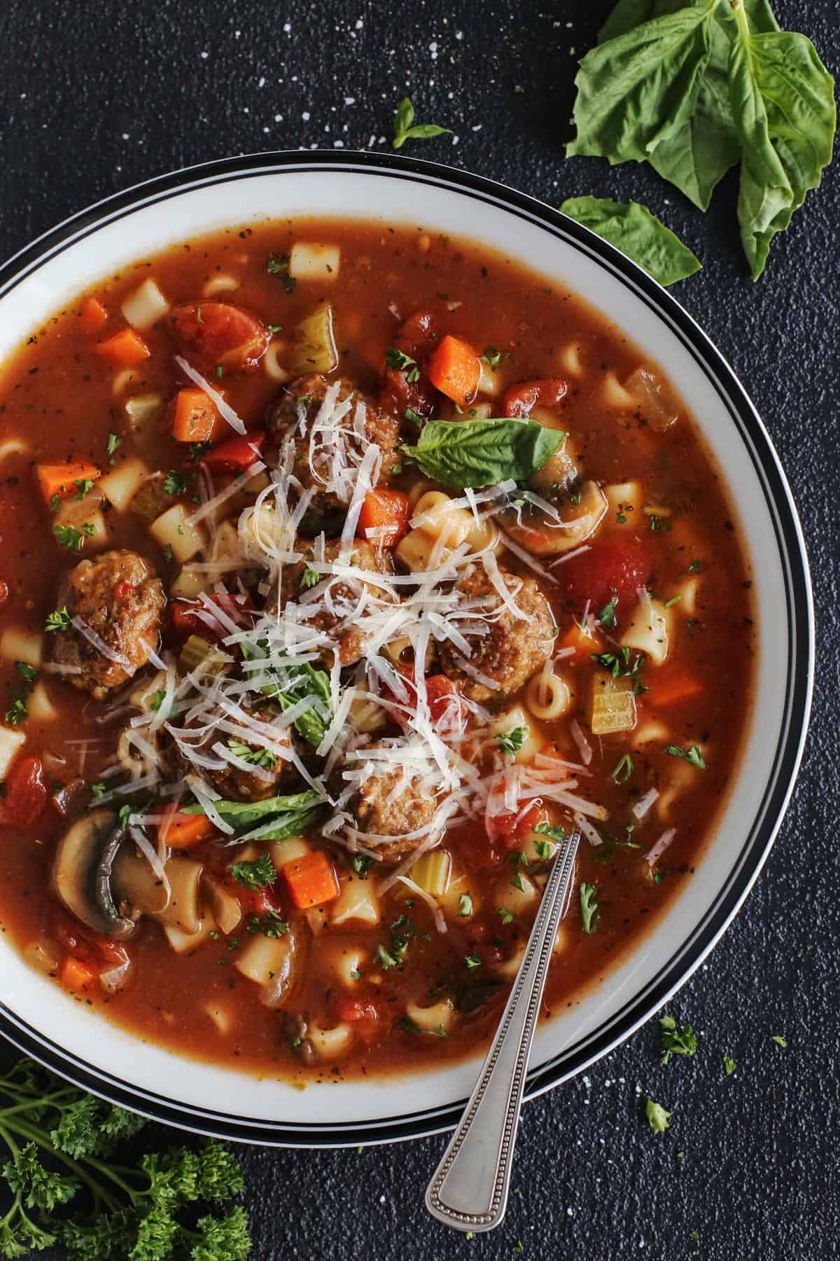 meatball soup in a white bowl, with fresh basil