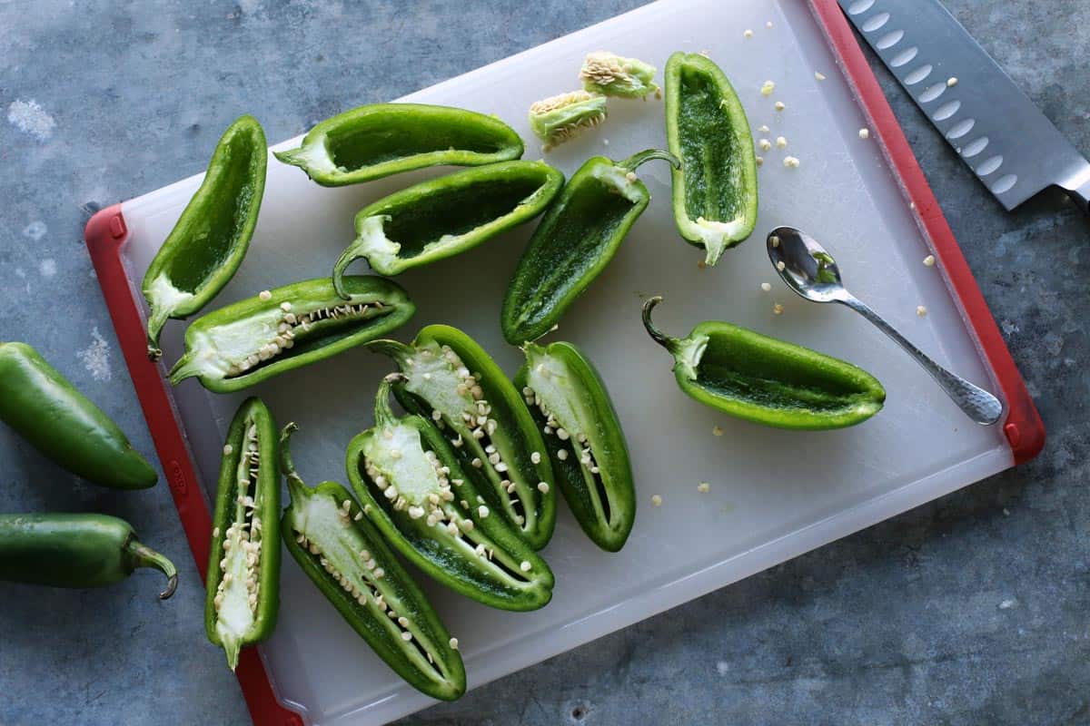 With Italian sausage, cream cheese, Parmesan, and mozzarella, these easy stuffed jalapeños are extra cheesy with the perfect amount of heat! Jalapeno peppers sliced in half, sitting on a cutting board
