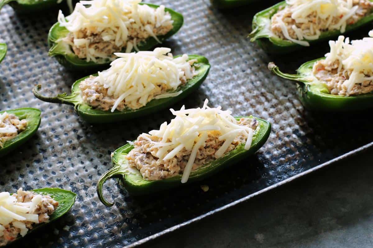 With Italian sausage, cream cheese, Parmesan, and mozzarella, these easy stuffed jalapeños are extra cheesy with the perfect amount of heat! roasted jalapeno halves on a pan, stuffed with Italian sausage, sprinkled with shredded mozzarella cheese