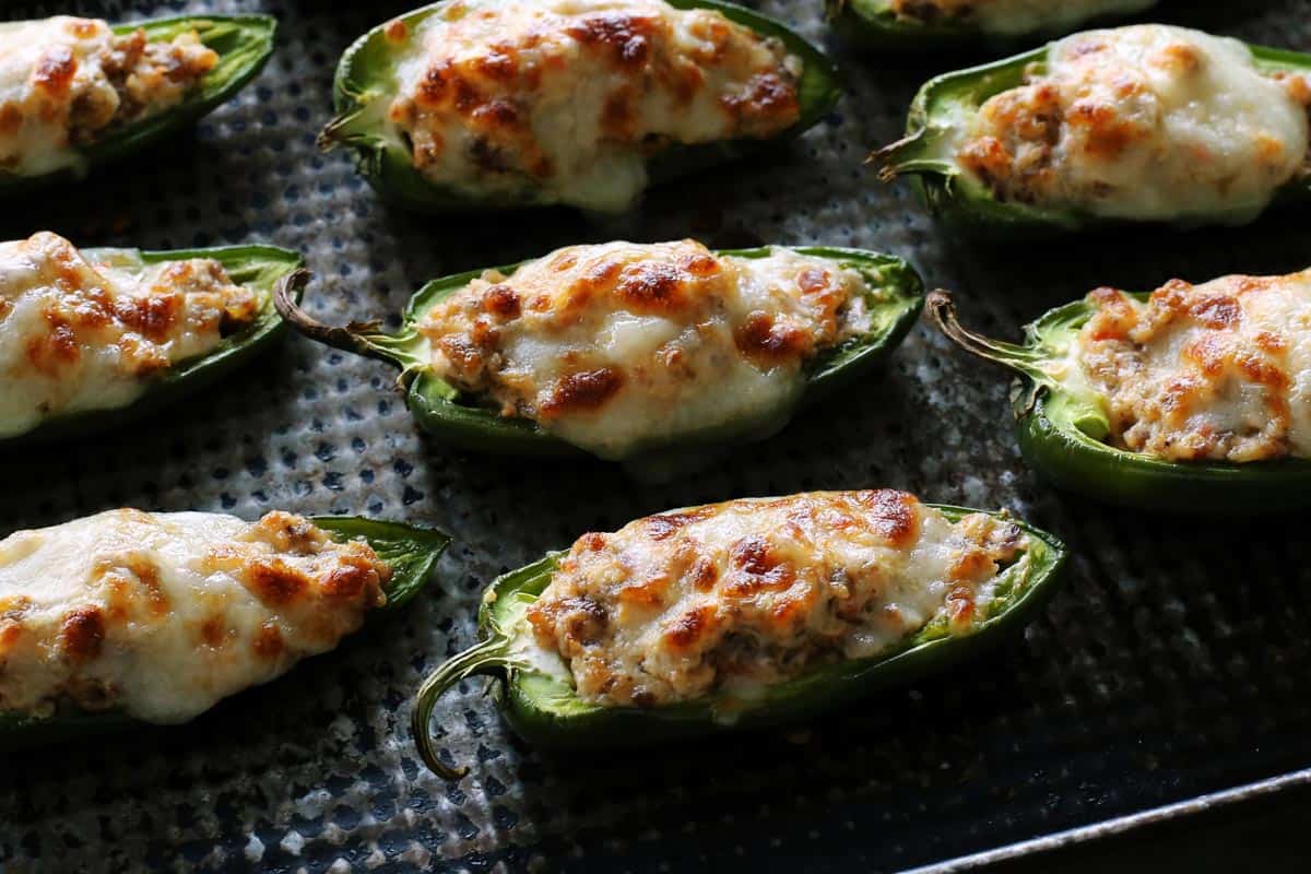 With Italian sausage, cream cheese, Parmesan, and mozzarella, these easy stuffed jalapeños are extra cheesy with the perfect amount of heat! baked stuffed jalapeno peppers baked on a pan